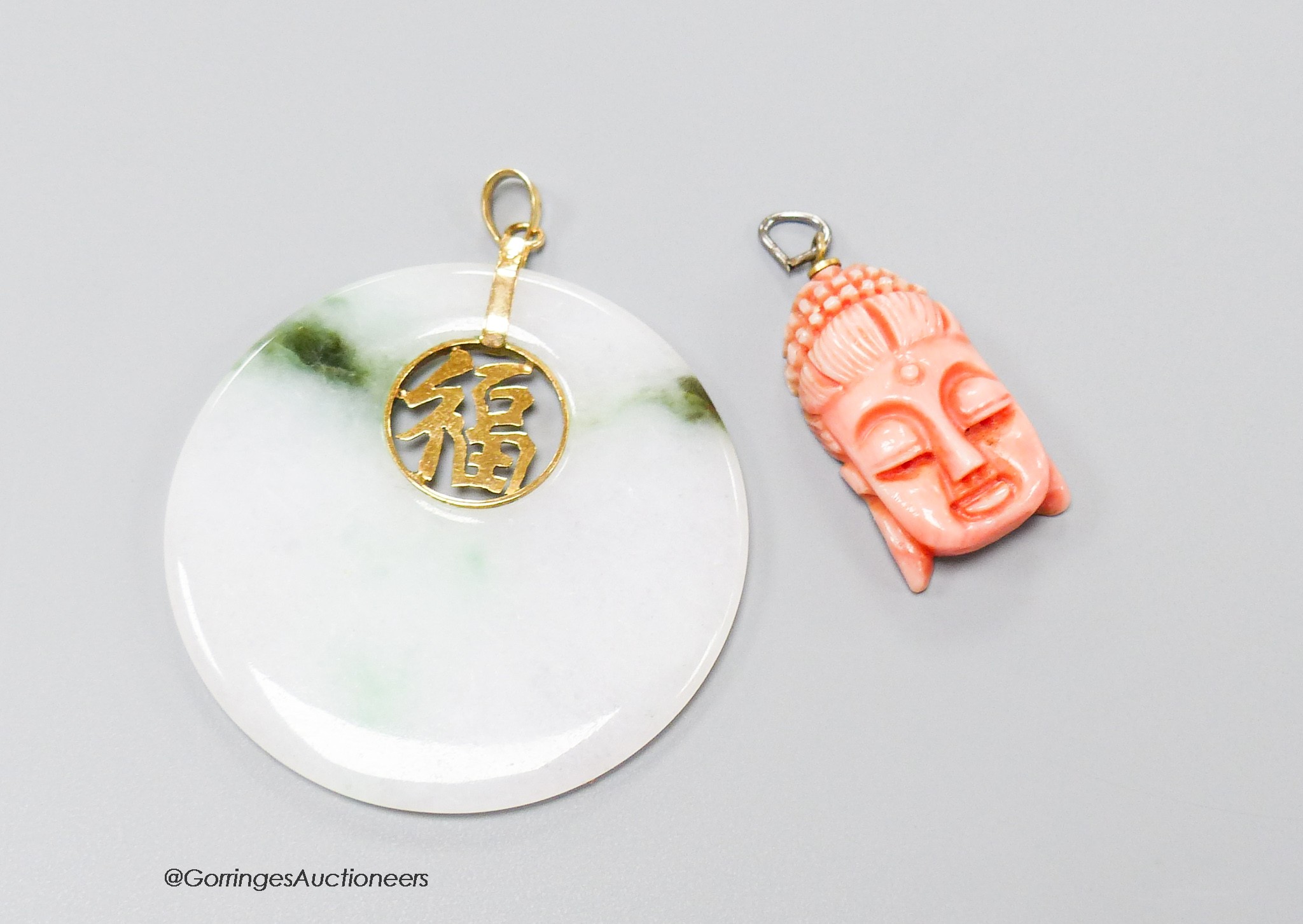 A Chinese jade disc pendant with inset yellow metal character and 14k bale, 46mm, and a carved coral mask pendant, 26mm.